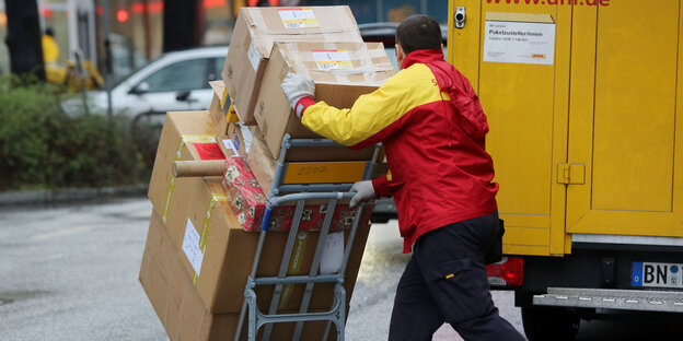 Paketbote schiebt eine Ladung Pakete von einem gelben Lastwagen weg Paketbote schiebt eine Ladung Pakete von einem gelben Lastwagen weg