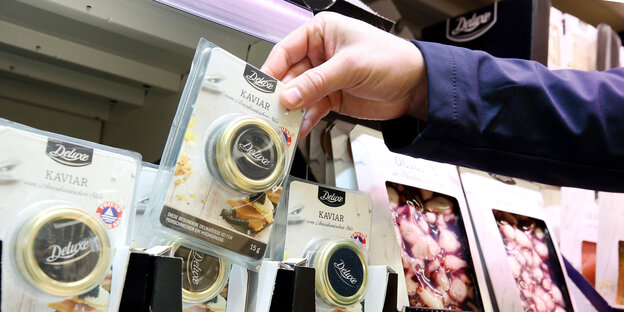 Eine Hand nimmt eine Kaviar-Packung aus dem Kühlregal Eine Hand nimmt eine Kaviar-Packung aus dem Kühlregal