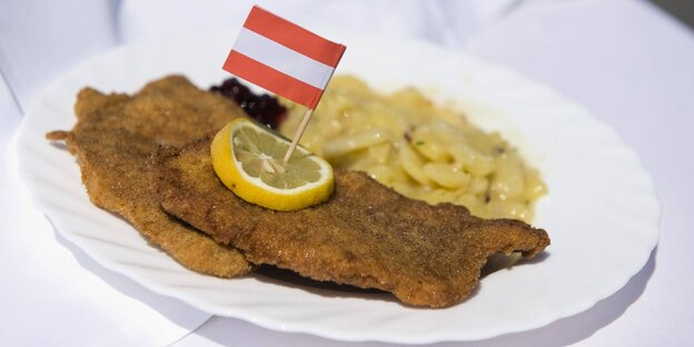 Zwei Schnitzel mit Kartoffelsalat auf einem Teller. Auf einem Schnitzel liegt eine Zitronenscheibe, dort reingesteckt eine Österreich-Fahne