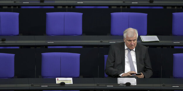 Bundesinnenminister Horst Seehofer sitzt im Bundestag und tippt auf seinem Handy, die blauen Stühle um ihn herum sind leer Bundesinnenminister Horst Seehofer sitzt im Bundestag und tippt auf seinem Handy, die blauen Stühle um ihn herum sind leer
