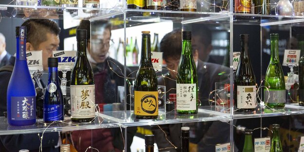 Mehrere Alkoholflaschen in verschiedenen Farben und mit japanischen Etiketten in einem Glasregal Mehrere Alkoholflaschen in verschiedenen Farben und mit japanischen Etiketten in einem Glasregal