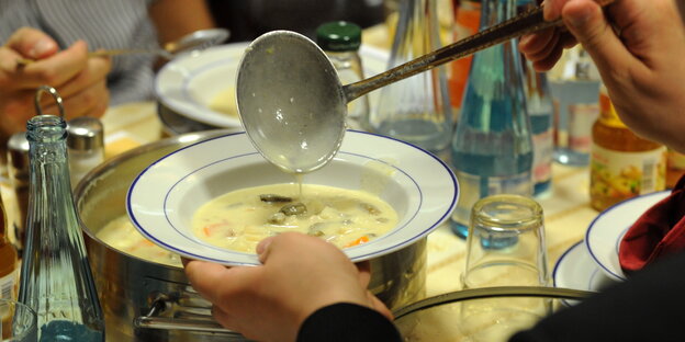 auf einem voll gedeckten Tisch schöpft jemand Suppe in einen Teller auf einem voll gedeckten Tisch schöpft jemand Suppe in einen Teller