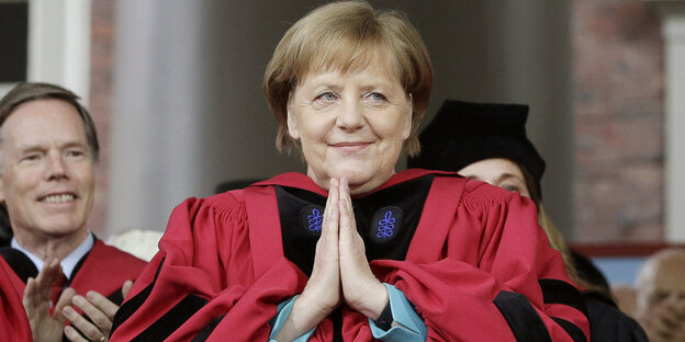 Angela Merkel trägt einen rot-schwarzen Talar und faltet ihre Hände Angela Merkel trägt einen rot-schwarzen Talar und faltet ihre Hände