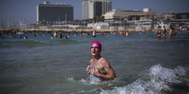 Eine Drag-Queen trägt eine pinkfarbene Bademütze und steht im Meer Eine Drag-Queen trägt eine pinkfarbene Bademütze und steht im Meer