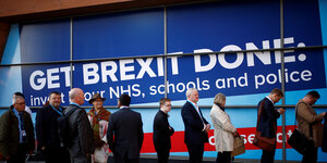 Wartende Parteitagsdelegierte vor einem großen blauen Plakat auf dem steht: Get Brexit Done