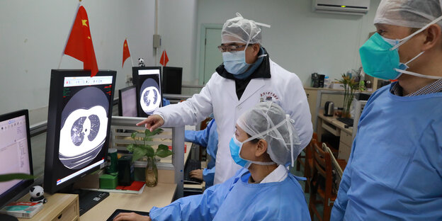 Drei Ärzte mit Mundschutz begutachten eine Comutertomographie