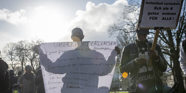 Zwei junge Männer halten auf der Demo von "Together we are Bremen" ein Plakat mit ihren Forderungen für Geflüchtete hoch. Eine davon: Keine Kriminalisierung von Minderjährigen