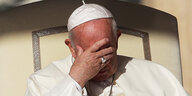 Papst Franziskus sitztend, hält sich schützend die Hand vor die Augen