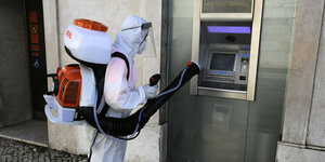 Eine Person in Schutzanzug desinfiziert einen Geldautomaten.