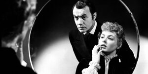 Die Schauspieler/innen Charles Boyer und Ingrid Bergman schauen in einen Spiegel