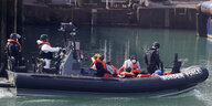 Ein Schlauchboot der britischen Grenzpolizei. In dem Boot befinden sich Polizisten und Geflüchtete. Die Polizisten tragen Schwimmwesten und Helme mit Visier. Die Geflüchteten nur Schwimmwesten.
