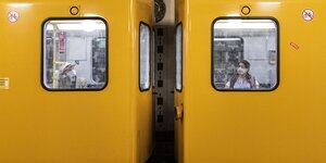 Zwei Menschen mit Mundschutz hinter den Fenstern zweier U-Bahn-Wagons