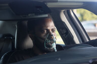 Ein Mann sitzt in einem Auto, über Mund und Nase eine mit einem Schlauch verbundene Maske