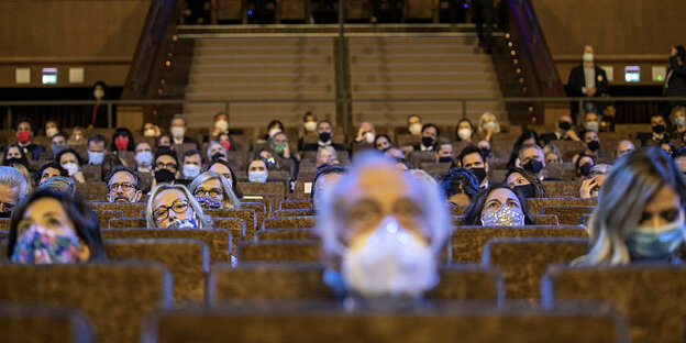 Menschen mit Atemschutzmasken sitzen in einem Kinosaal