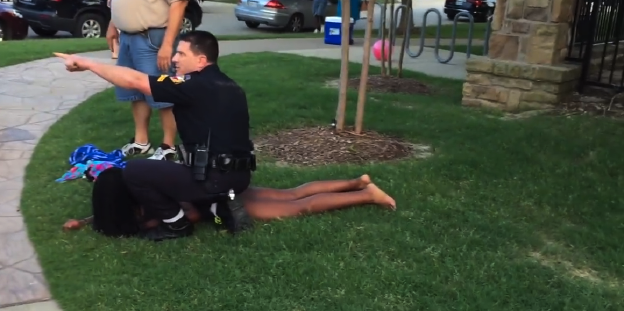 Ein Mädchen wird von einem Polizisten auf den Boden gedrückt