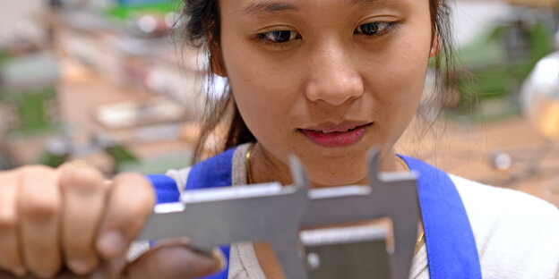 Eine junge Vietnamesin in einer Werkstatt. Sie misst ein Werkstück aus. Eine junge Vietnamesin in einer Werkstatt. Sie misst ein Werkstück aus.