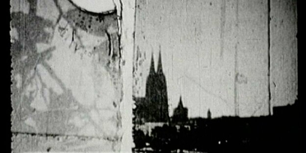 Schwarzweißes Filmbild, beschädigte Oberfläche, erkennbar ist die Silhouette des Kölner Doms