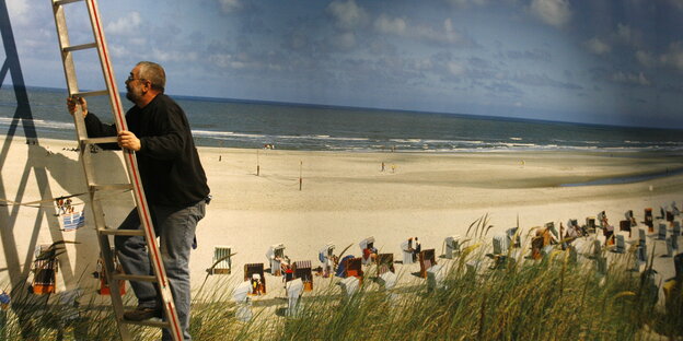 Mann steigt am Strand auf eine Leiter Mann steigt am Strand auf eine Leiter
