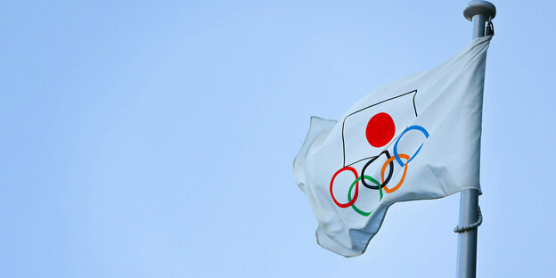 Japanische Flagge mit Olympia-Ringen weht am Mast vor blauem Himmel