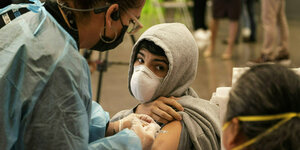 Ein Schüler blick zu seiner Mutter, während er geimpft wird