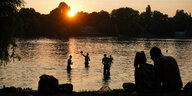 Im Sonnenuntergang spielen einige Menschen Ball im Wasser