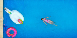 Ein Mädchen schwimmt im Gartenpool mit Einhorn, Schwimmreifen und Delfin