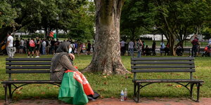 Auf einer Bank sitzt eine Frau mit Schleier. Im Hintergrund stehen Menschen vor dem Zaun des Weißen Hauses in Washington