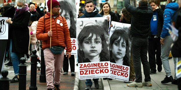 Protestirende tragen zwei große Plakate mit dem Foto eines kleinen Mädchens