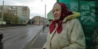 Alte Frau steht an Straßenrand