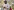 Der Rapper Akon steht in einer Moschee und Betet. Er trägt ein gediegenes Hemd in Grauton und hat die Hände unter der Brust übereinandergeschlagen. Er trägt eine Maske. Im Hintergrund weitere Männer.