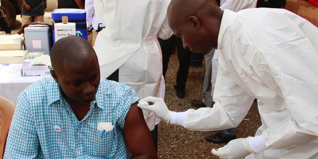 Ein Mediziner impft einen Patienten in Conakry, Guinea