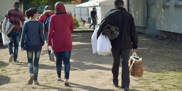 Flüchtlinge mit Bettzeug in der Hand gehen einen Weg entlang Flüchtlinge mit Bettzeug in der Hand gehen einen Weg entlang