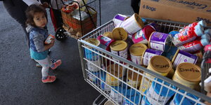 Ein Kind steht neben einem mit Babymilch gefüllten Einkaufswagen
