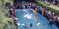Eine Menschenmenge steht um einen Swimmingpool herum, viele sind im Wasser