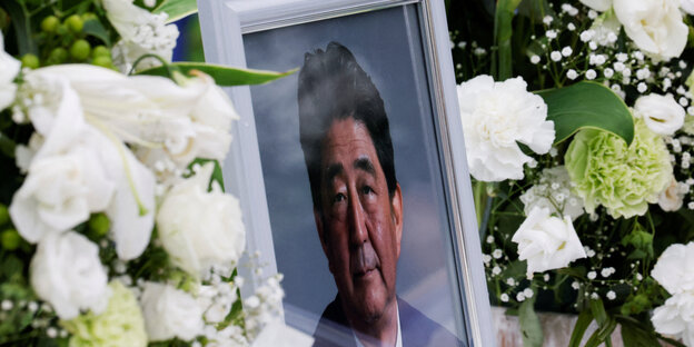 Foto von Shinzō Abe in einem Bilderahmen, der in weißen Blumen steckt.