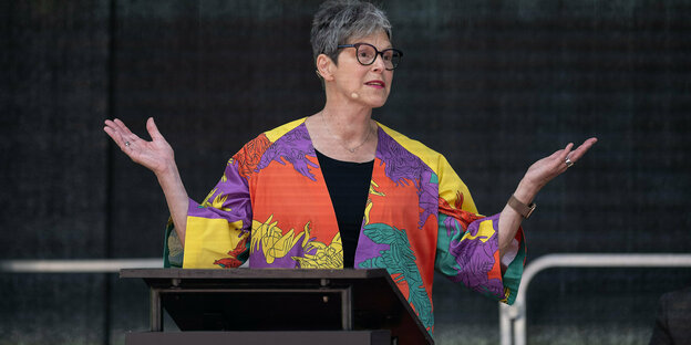 Eine Frau mit kurzen grauen Haaren gestikuliert an einem Redepult