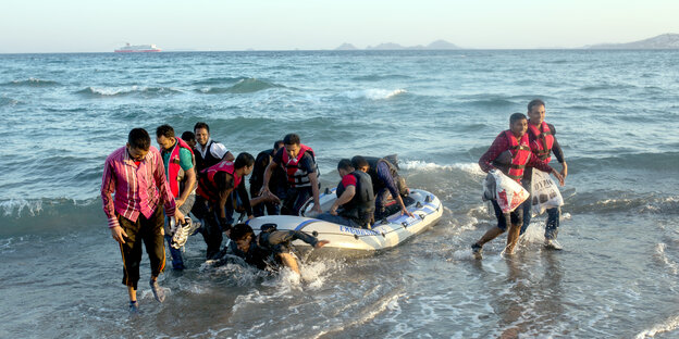 Menschen mit Schwimmwesten springen von einem Schlauchboot auf den Strand Menschen mit Schwimmwesten springen von einem Schlauchboot auf den Strand