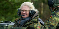Verteidigungsminsiterin Lambrecht in tarnfarbener Uniform mit Ohrschutz auf einem Panzer