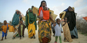 Eine Gruppe von Frauen und Kindern geht durch staubiges Gelände