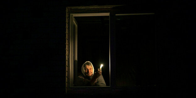Eine Frau hält eine Kerze und blickt aus dem Fenster bei tiefster Nacht