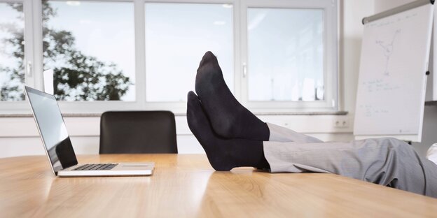Männerbeine und -füße auf dem Schreibtisch, vor Laptop Männerbeine und -füße auf dem Schreibtisch, vor Laptop