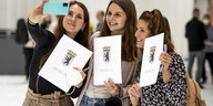 Drei junge Lehrerinnen mit Urkunden posieren für ein Selfie