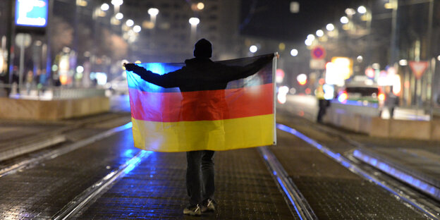 Ein Anhänger der Pegida-Bewegung steht mit einer deutschen Fahne in Dresden auf der Straße. Ein Anhänger der Pegida-Bewegung steht mit einer deutschen Fahne in Dresden auf der Straße.