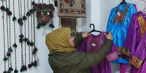 Eine Frau hängt bunte Kleidung an einem Marktstand auf