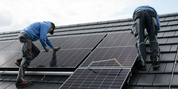 Zwei Männer montieren eine Solaranlage auf ein Hausdach