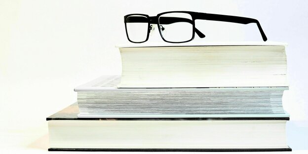 Eine Brille mit schwarzem Gestell liegt auf einem Stapel Bücher