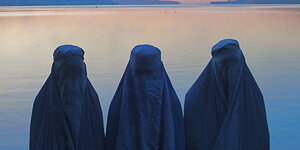 Drei Personen mit burkas vor einem See