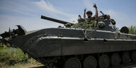 Soldaten sitzen auf einem Panzer. Einer von ihnen zeigt mit beiden Händen das Victory-Zeichen