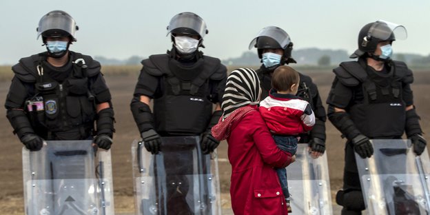 Eine Frau mit einem Kind geht in Roszke an einer Reihe von Polizisten vorbei