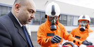 Nouiripour schuat auf Materialine von 2 Katastrophenschützern mit Atemschutzmasken und orangen Anzügen
